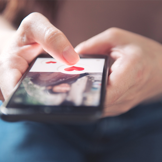 Finger of woman pushing heart icon on screen in mobile smartphone application. Online dating app, valentine’s day concept.